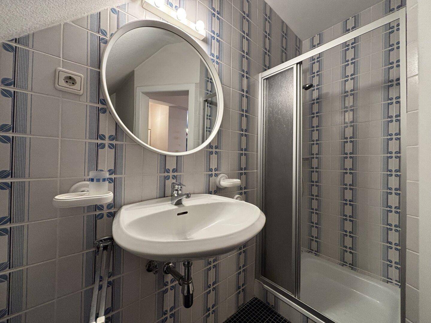 Badezimmer im Dachgeschoss mit Dusche, Waschbecken und blau-weiß gemusterten Fliesen.