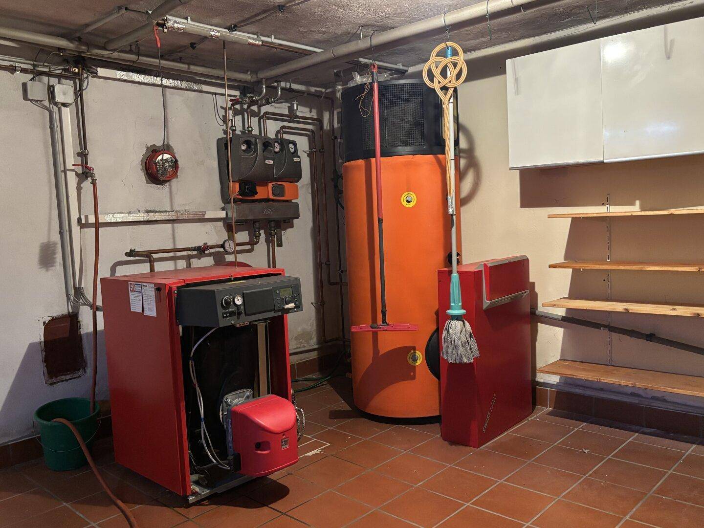 Heizungsraum im Keller mit Heizungsanlage, Warmwasserspeicher und Regalen.