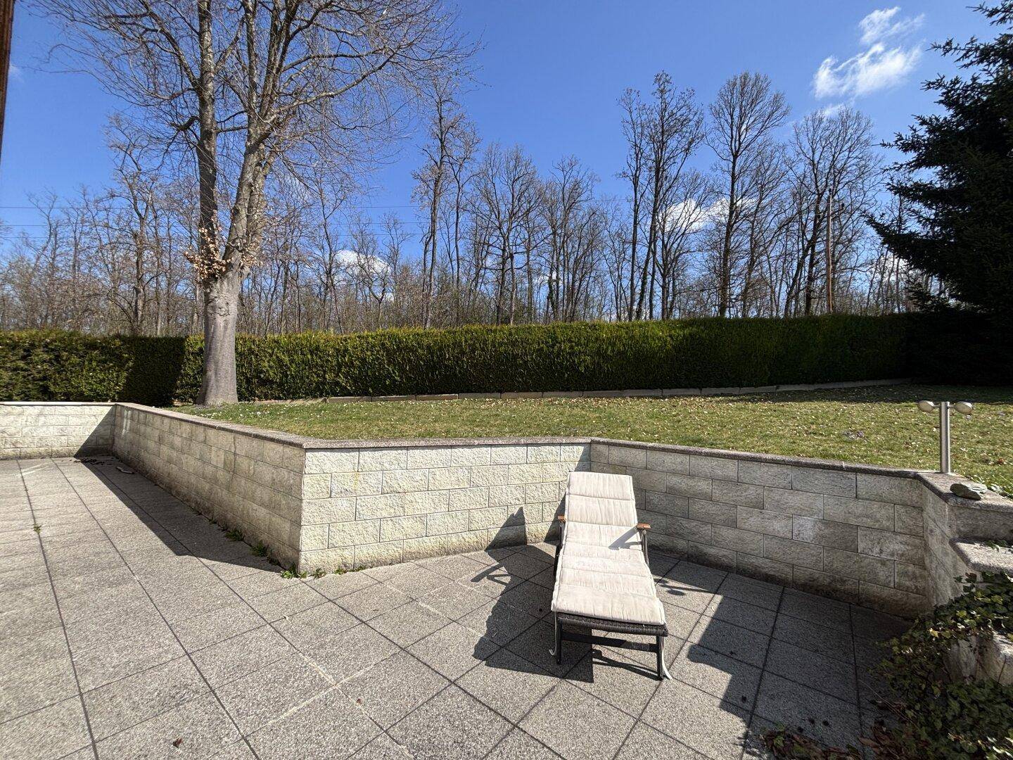 Sonniger Terrassenbereich mit Liegestuhl, Steinmauern und Blick ins Grüne.