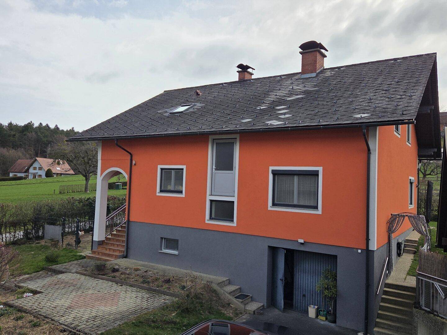 Rückansicht des Hauses mit orangefarbener Fassade, Satteldach und Zugang zum Kellergeschoss.