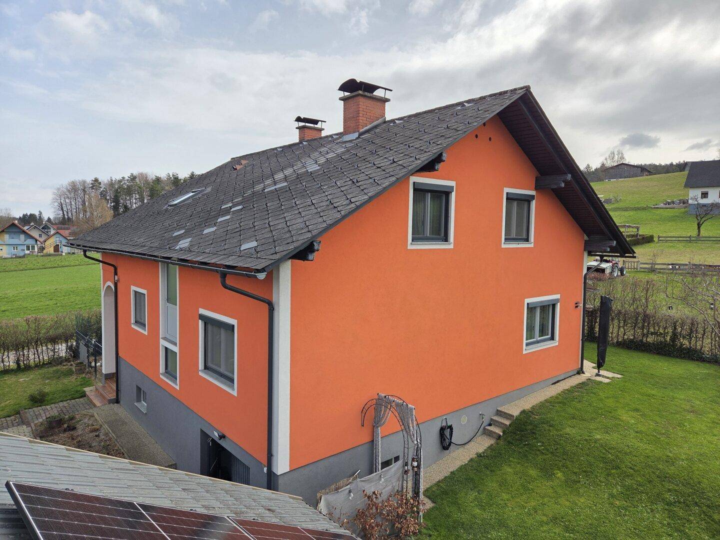Seitenansicht des orangefarbenen Hauses mit Satteldach und grüner Rasenfläche im Vordergrund.