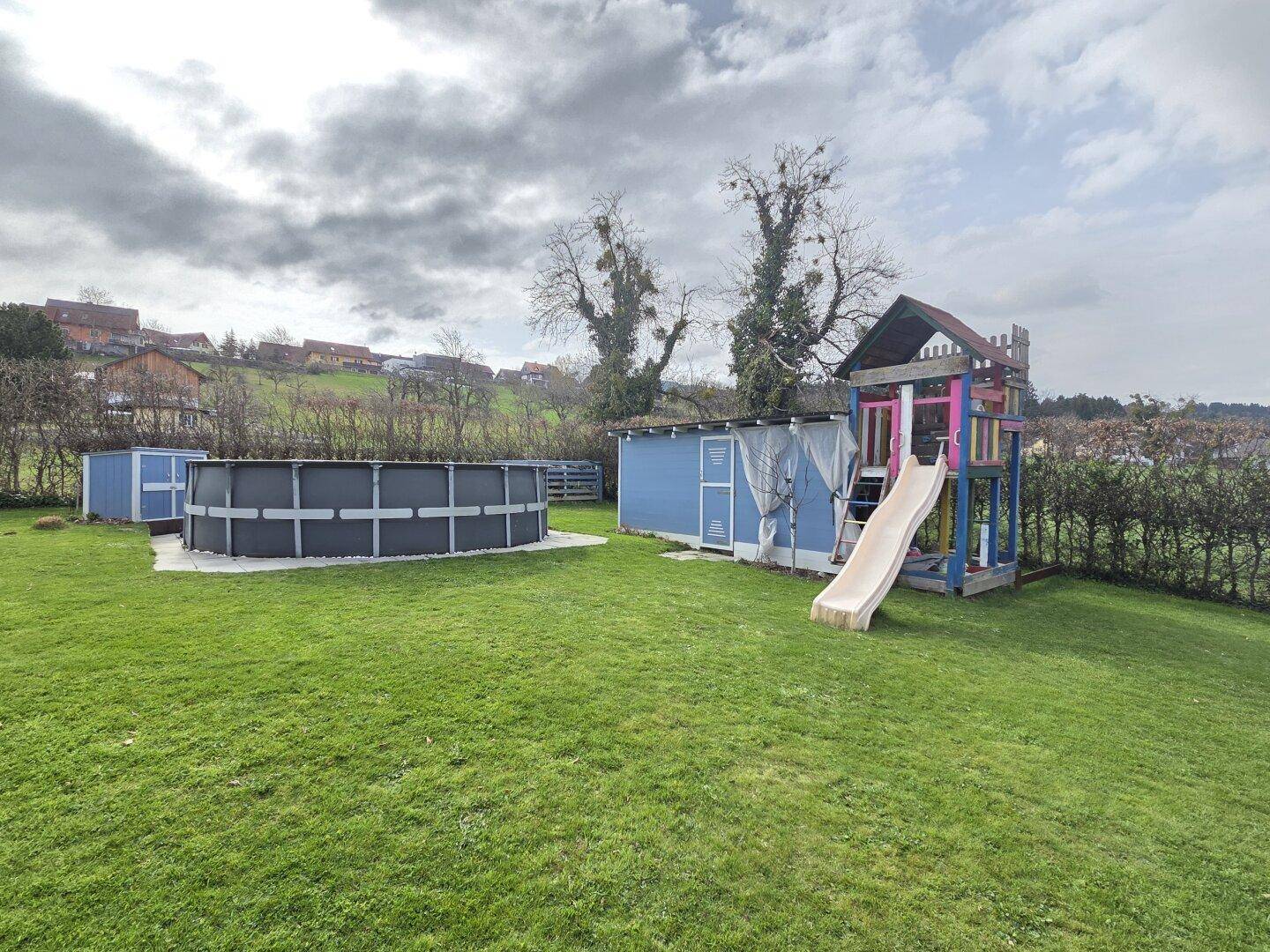 Großer Garten mit Rasenfläche, einem Aufstellpool und einem Kinderspielplatz mit Rutsche.