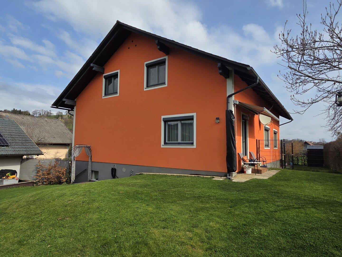 Seitenansicht des Hauses mit kleiner Terrasse und Zugang zum Garten, umgeben von Rasen.