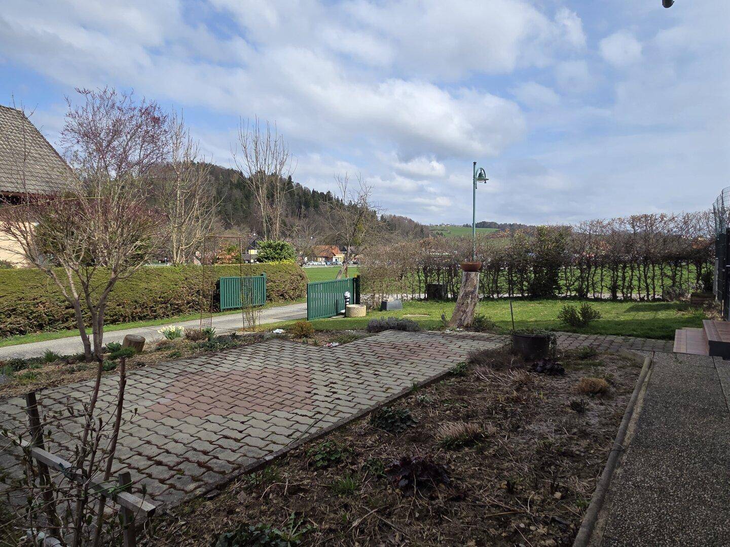 Vorgarten mit gepflastertem Bereich und Blick auf die umliegende Landschaft und Häuser.
