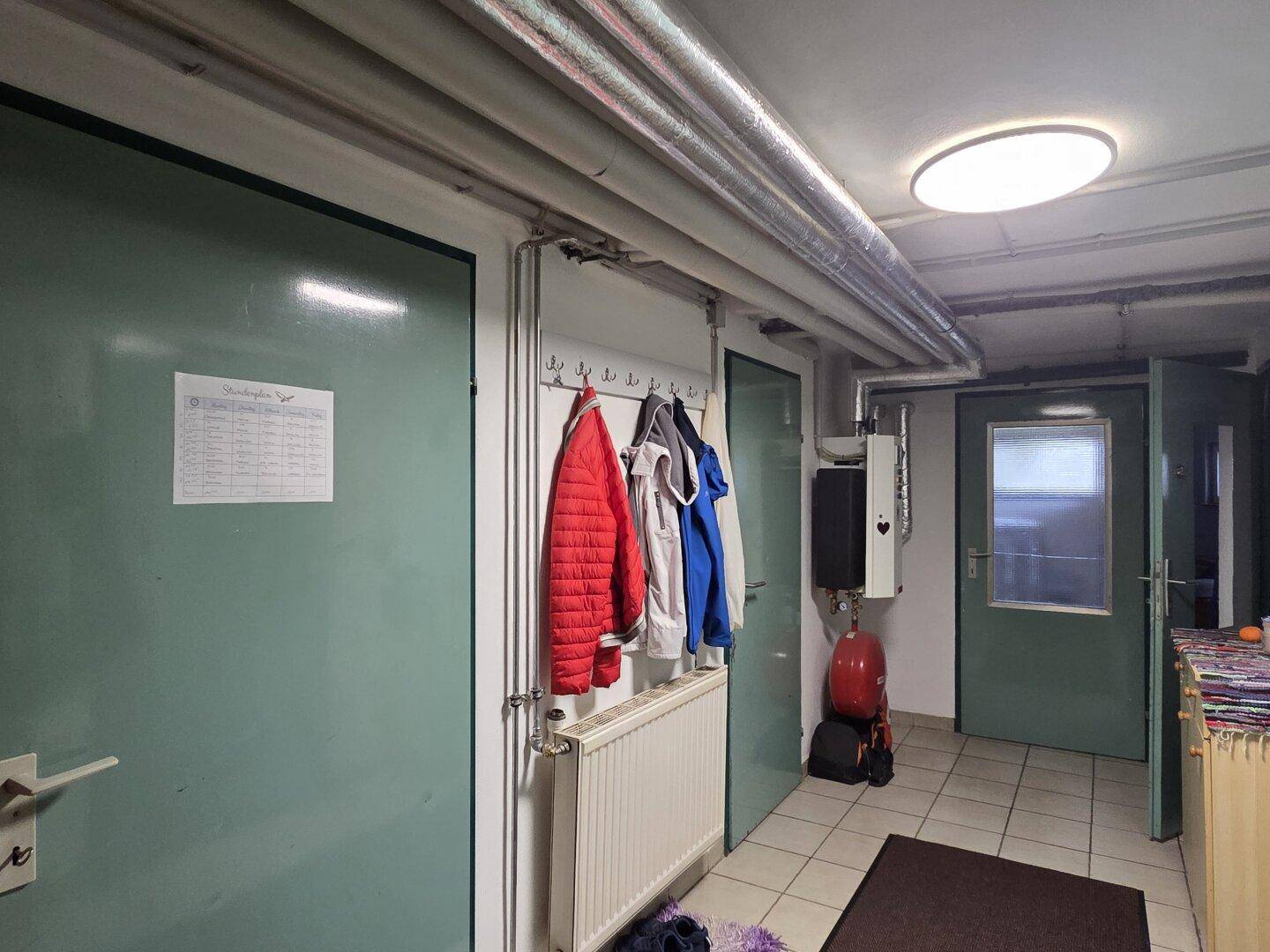 Kellerflur mit Heizkörper, Garderobe und mehreren Türen, die zu verschiedenen Räumen führen.
