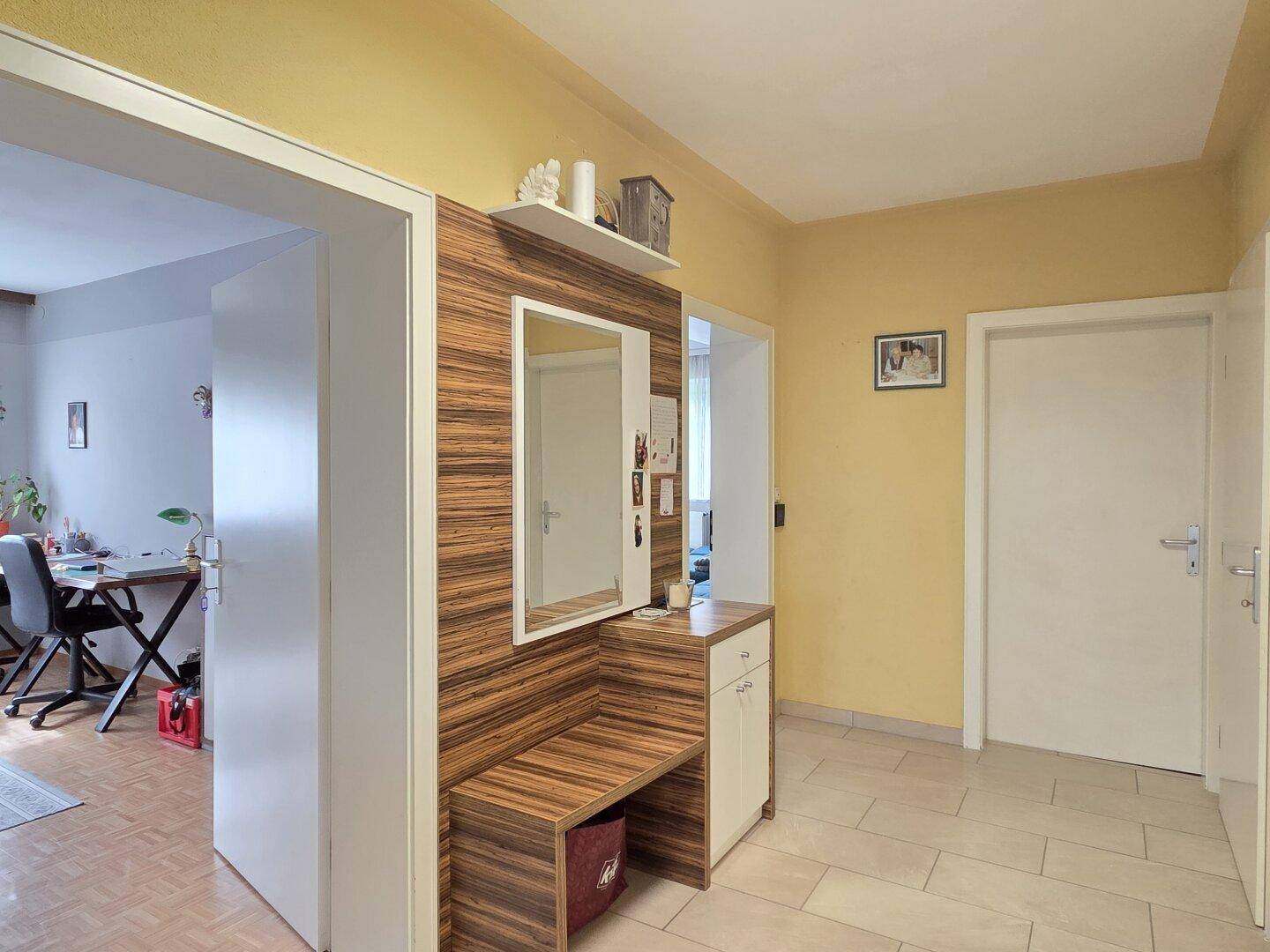 Heller Flur mit gelben Wänden, Fliesenboden und einem modernen Garderobenbereich mit Spiegel.