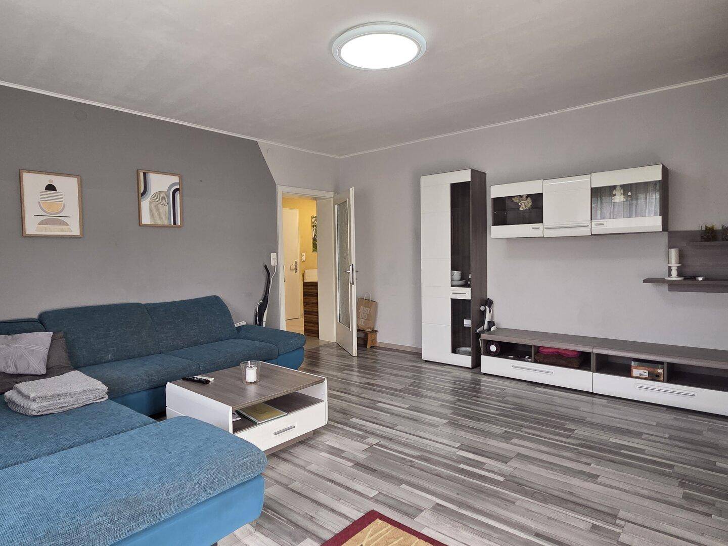 Helles Wohnzimmer mit modernem Sofa, Laminatboden und einer Medienwand mit Stauraum.