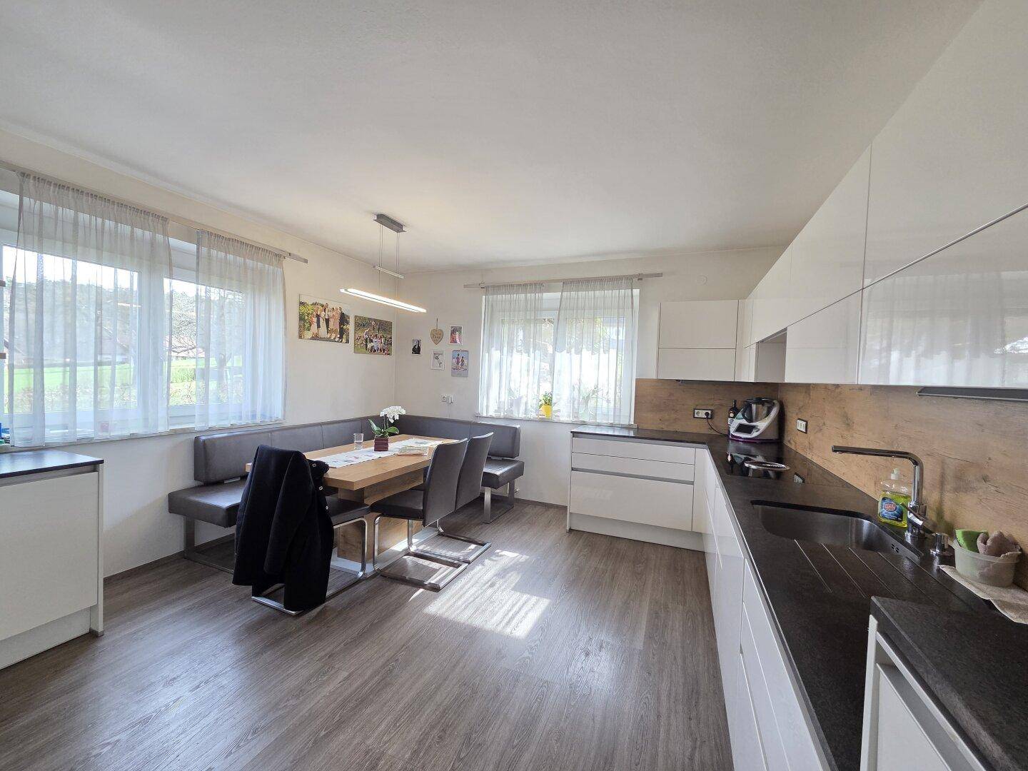 Moderne Wohnküche mit weißen Schränken, dunkler Arbeitsplatte und einem gemütlichen Essbereich mit Eckbank.