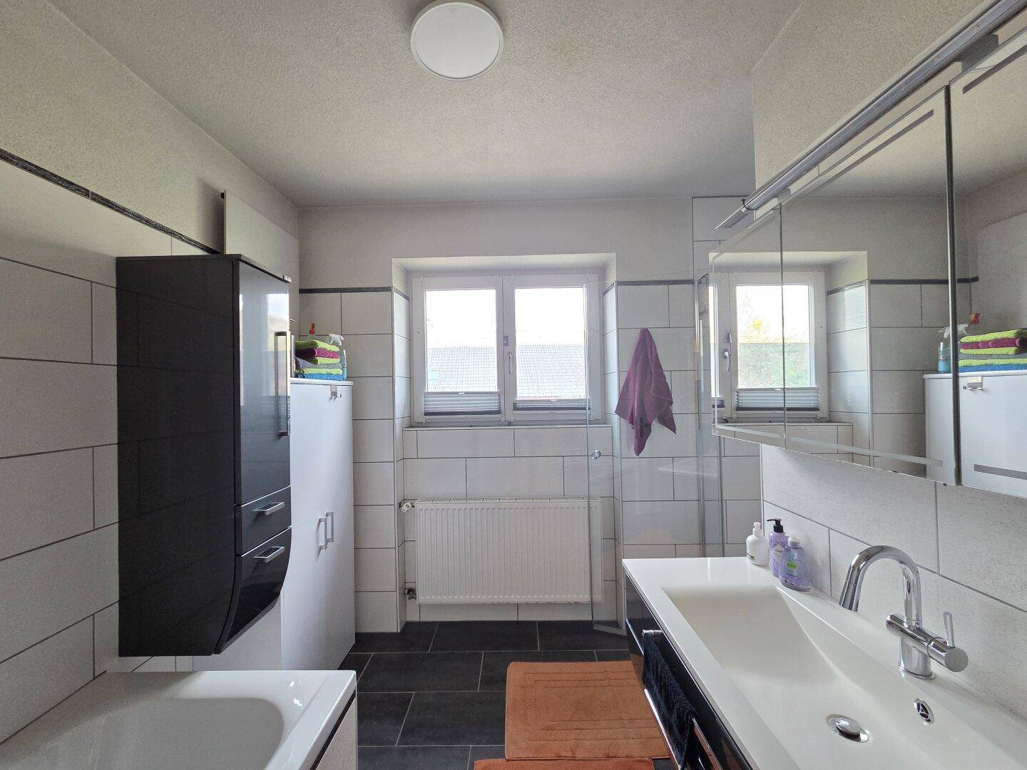 Modernes Badezimmer mit weißen Fliesen, dunklem Boden und einem Waschbecken mit Spiegelschrank.