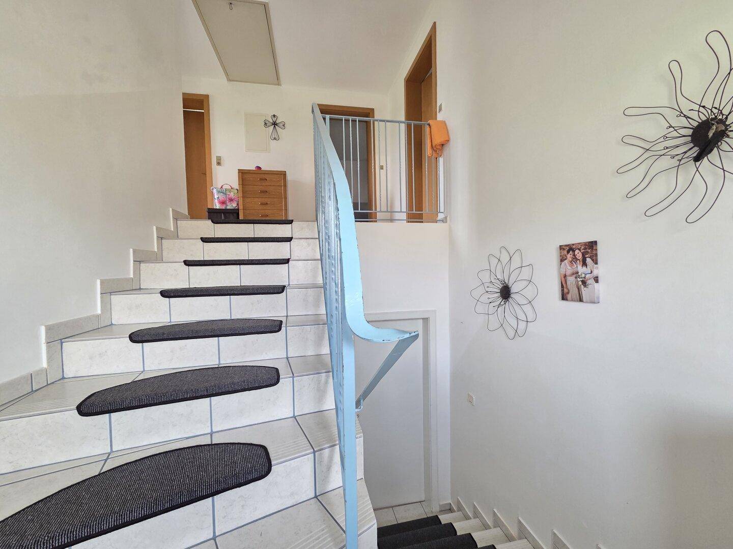 Treppenhaus mit gefliesten Stufen und einem blauen Geländer, das in die obere Etage führt.