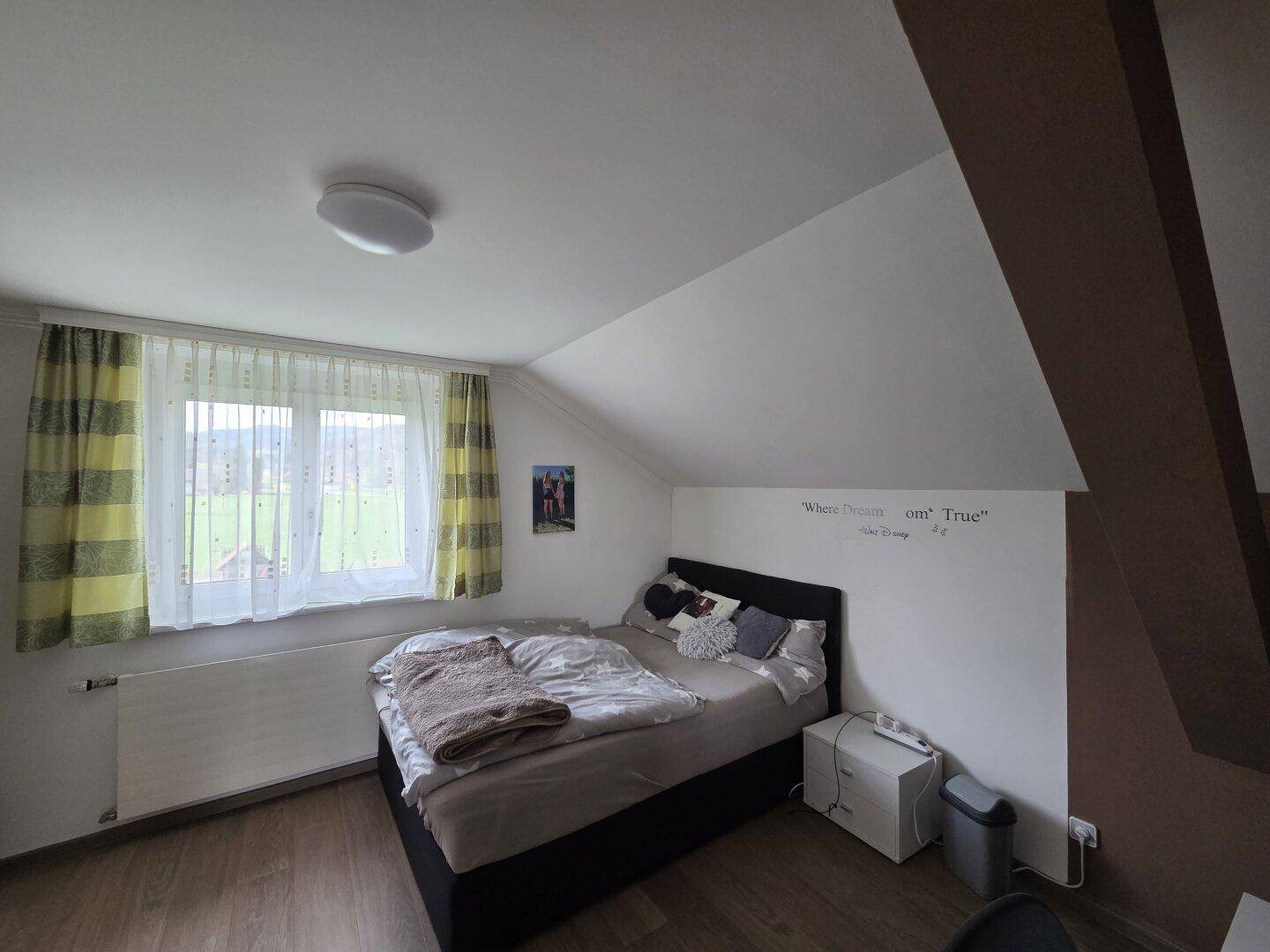 Gemütliches Schlafzimmer im Dachgeschoss mit Schrägen, Laminatboden und Fenster mit grüner Aussicht.