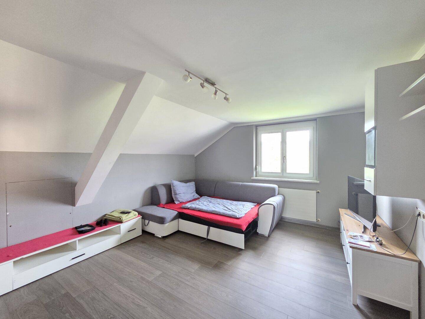 Wohnbereich im Dachgeschoss mit Schrägen, Sofa und Laminatboden, ideal als Gästezimmer nutzbar.