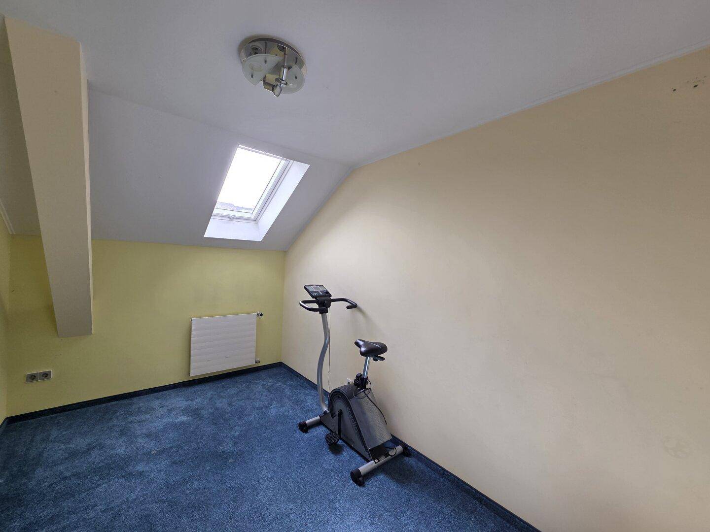 Raum im Dachgeschoss mit Schrägen, Teppichboden und einem Dachfenster, genutzt als Fitnessbereich.