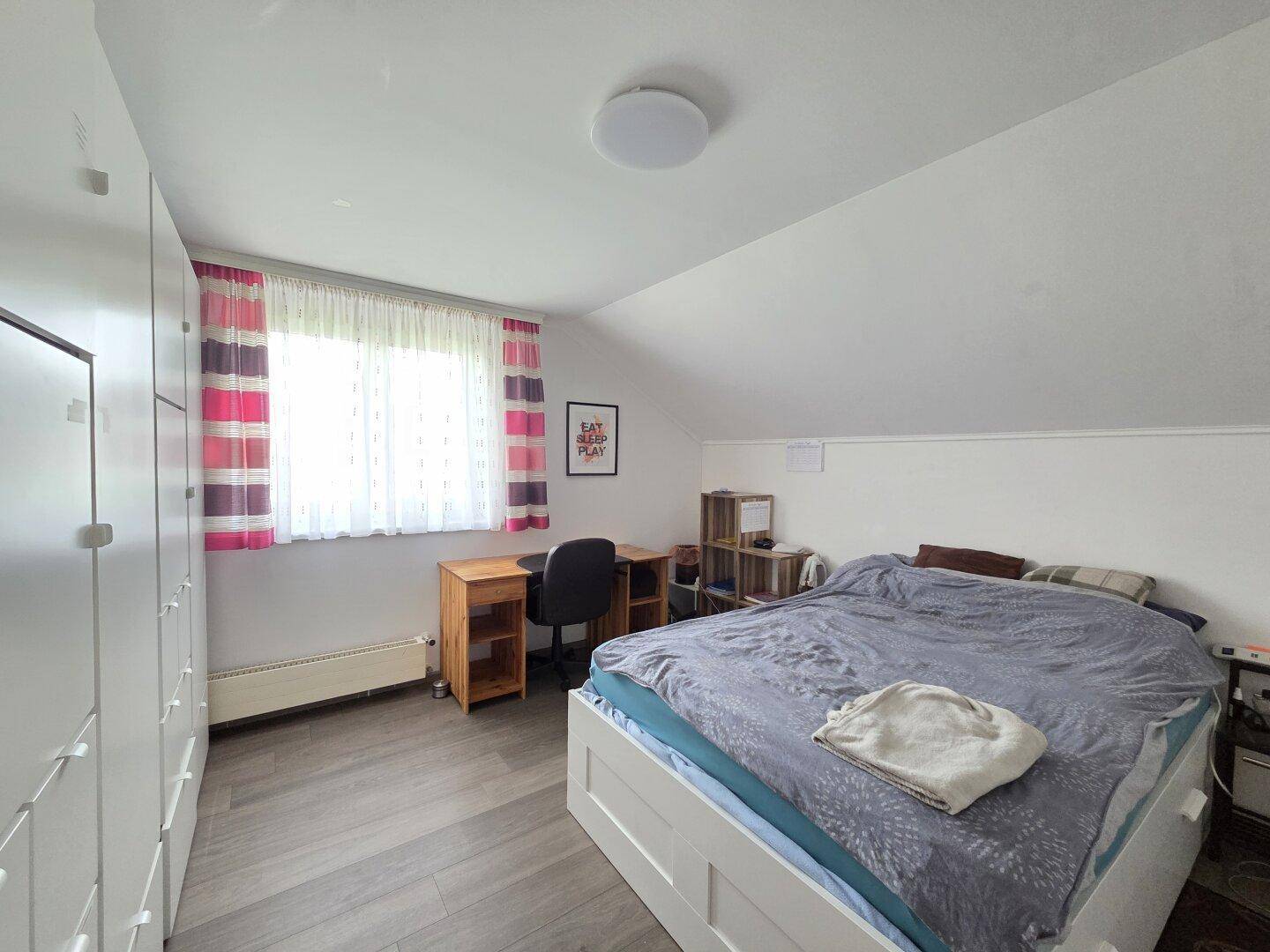 Helles Schlafzimmer im Dachgeschoss mit Schrägen, Laminatboden und großem Fenster.