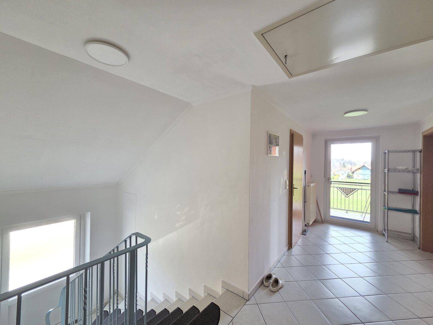 Geräumiger Flur im Obergeschoss mit Fliesenboden und Zugang zu einem Balkon mit Weitblick.