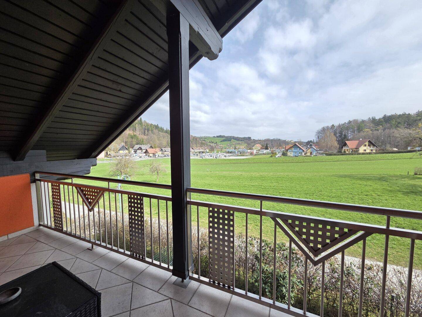 Balkon mit Metallgeländer und Fliesenboden, bietet einen weiten Blick auf die grüne Landschaft.