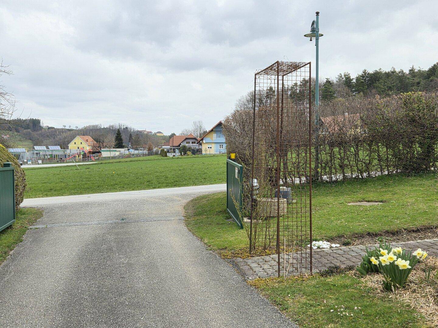 Zufahrt zum Grundstück mit einem grünen Tor und einem gepflasterten Weg, umgeben von Rasen.