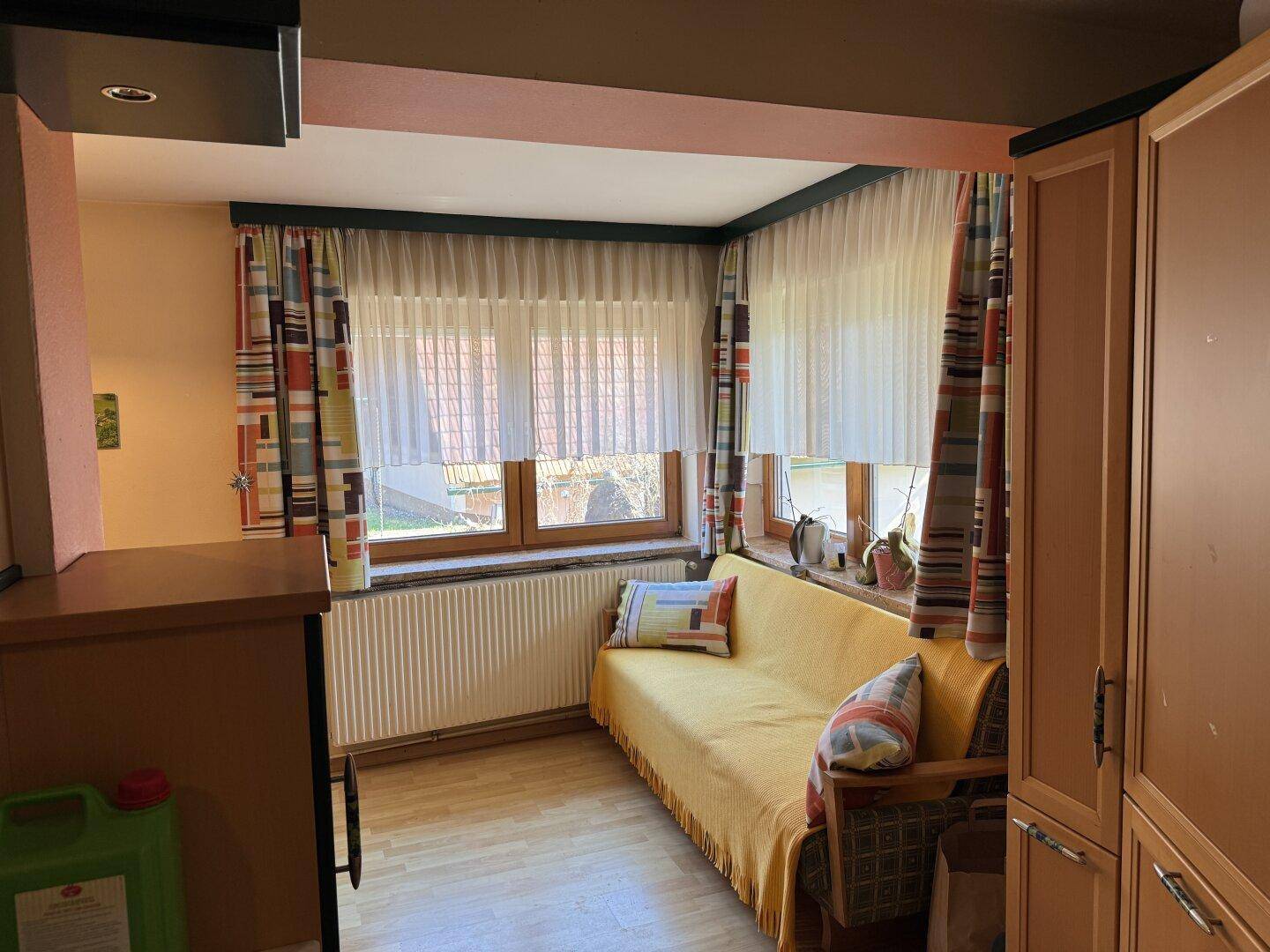 Heller Wohnbereich mit Sofa, großen Fenstern und farbenfrohen Vorhängen.
