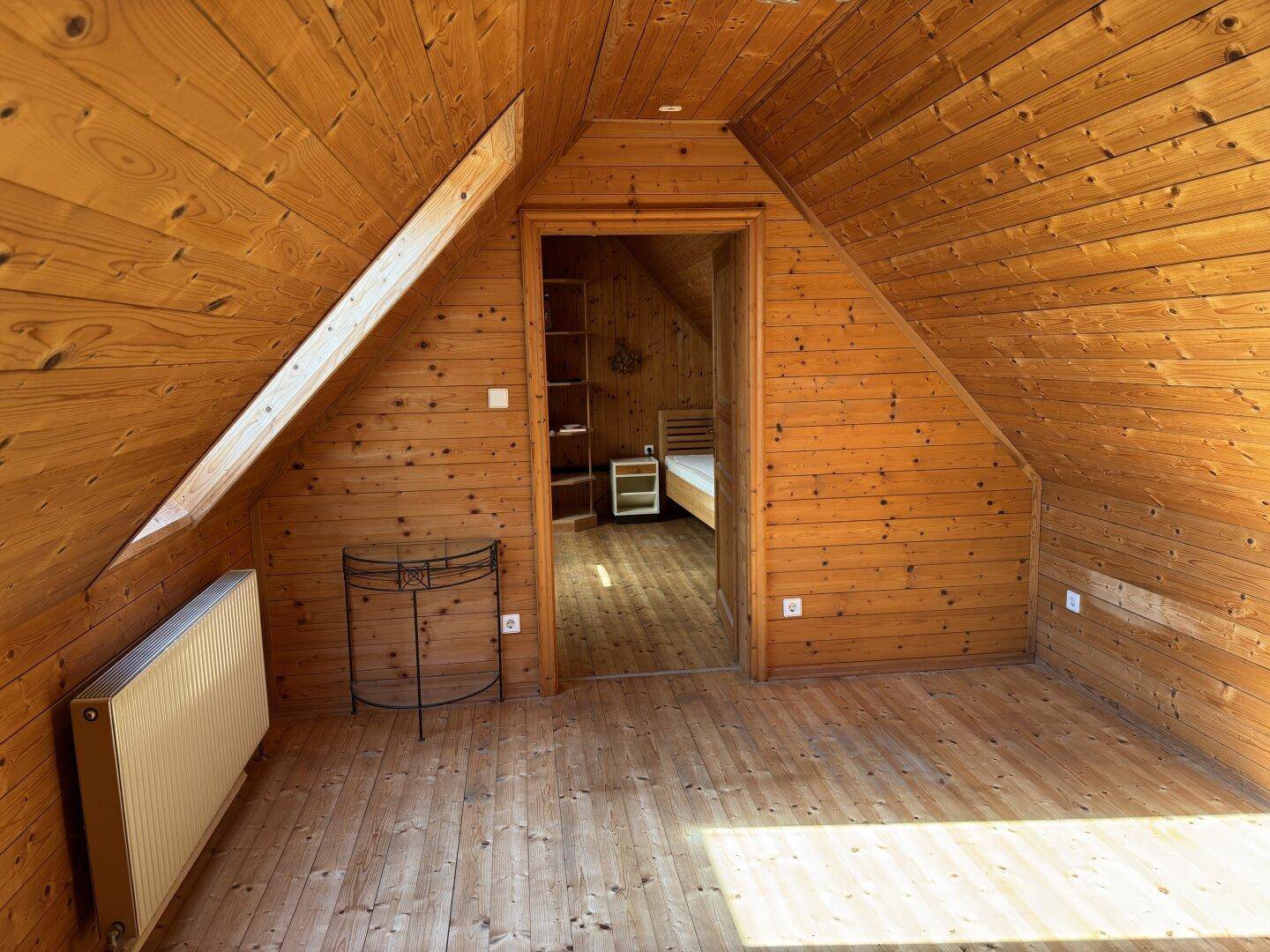 Rustikaler Dachbodenraum mit Holzverkleidung und Zugang zu einem weiteren Schlafzimmer.