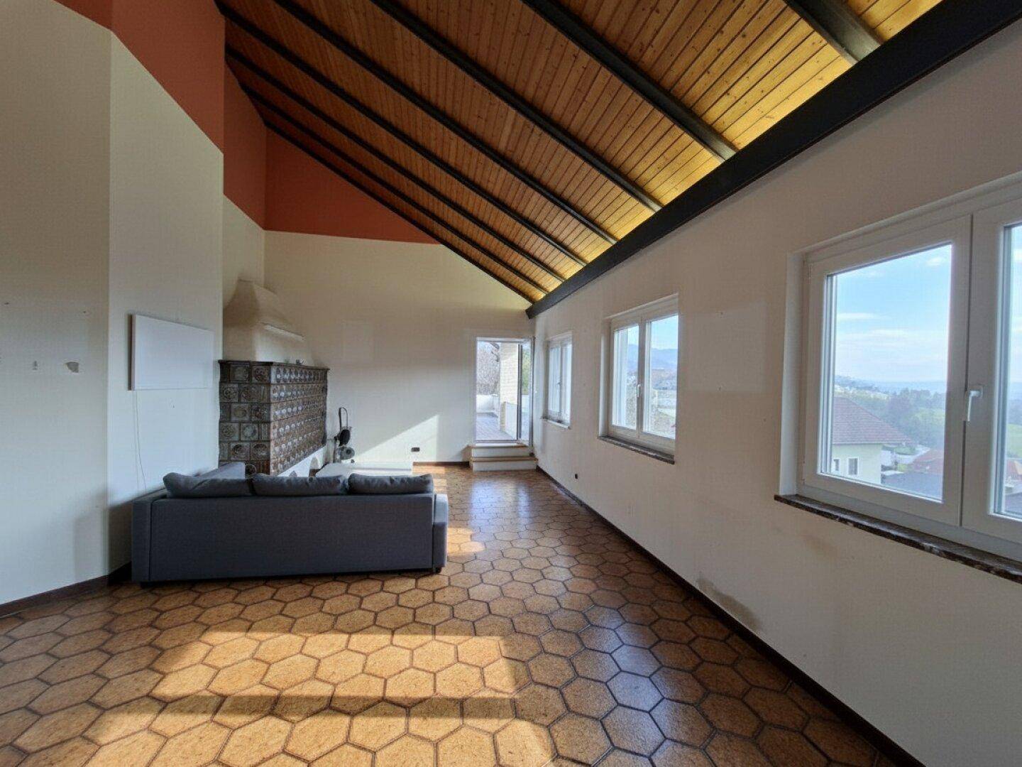 Geräumiges Wohnzimmer mit Holzbalkendecke, Kachelofen und großen Fenstern mit Weitblick.