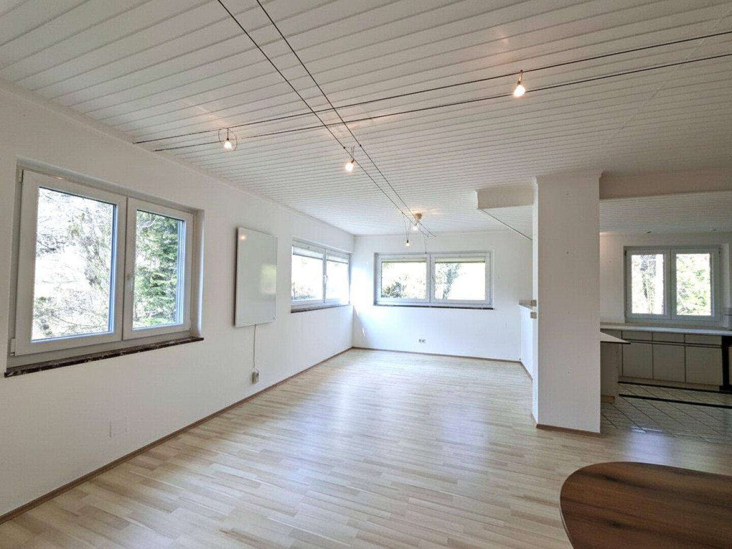 Helles Zimmer mit Holzparkettboden und mehreren Fenstern, die den Raum gut belichten.