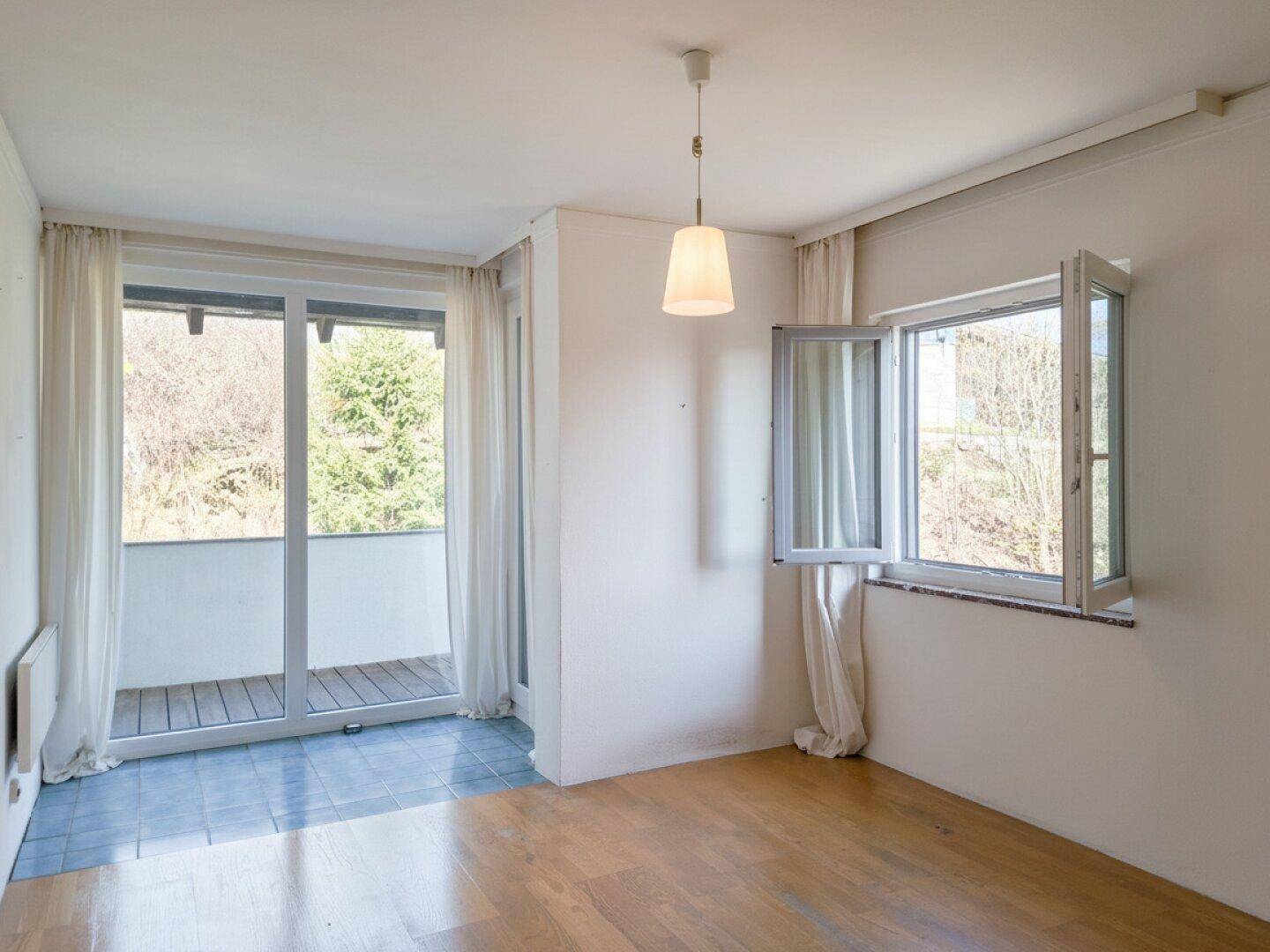 Zimmer mit Holzboden, Balkonzugang und großen Fenstern für viel Tageslicht.