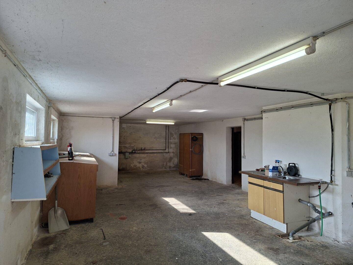 Geräumiger Kellerraum mit Fenstern, Betonboden und einfacher Ausstattung.
