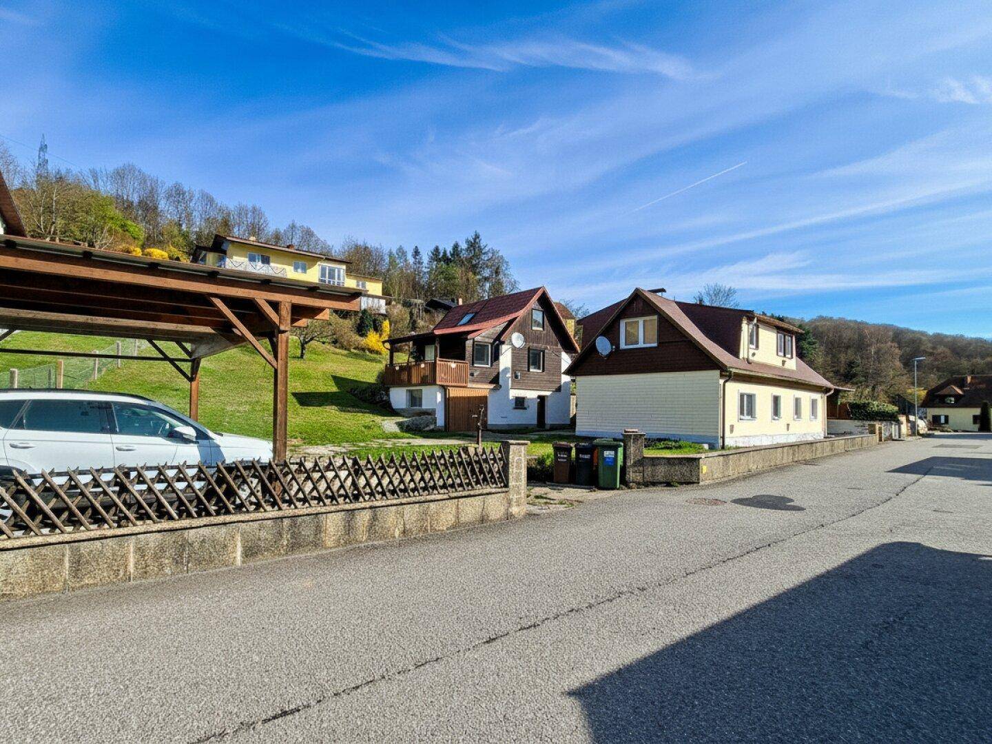 Straßenansicht mit Wohnhäusern, einem Carport und gepflegten Vorgärten unter blauem Himmel.