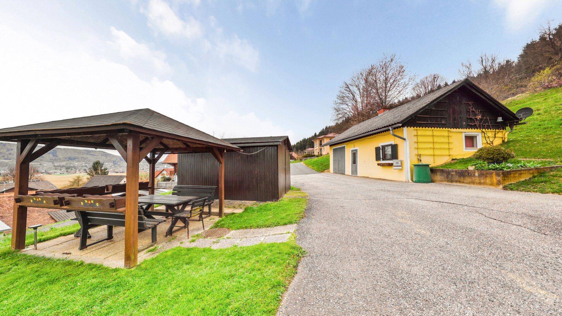 Gemütlicher Holzpavillon mit Sitzgelegenheiten und Grillplatz, umgeben von grüner Natur.