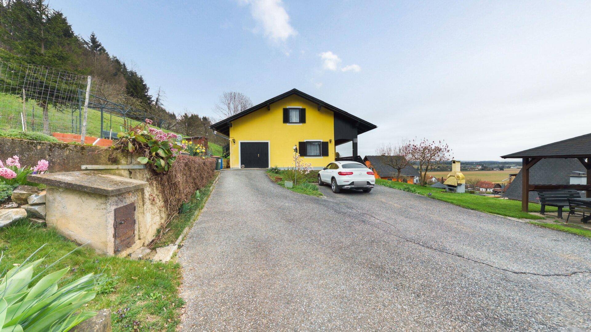 Gelbes Einfamilienhaus mit Garage und Auffahrt, umgeben von grüner Natur.