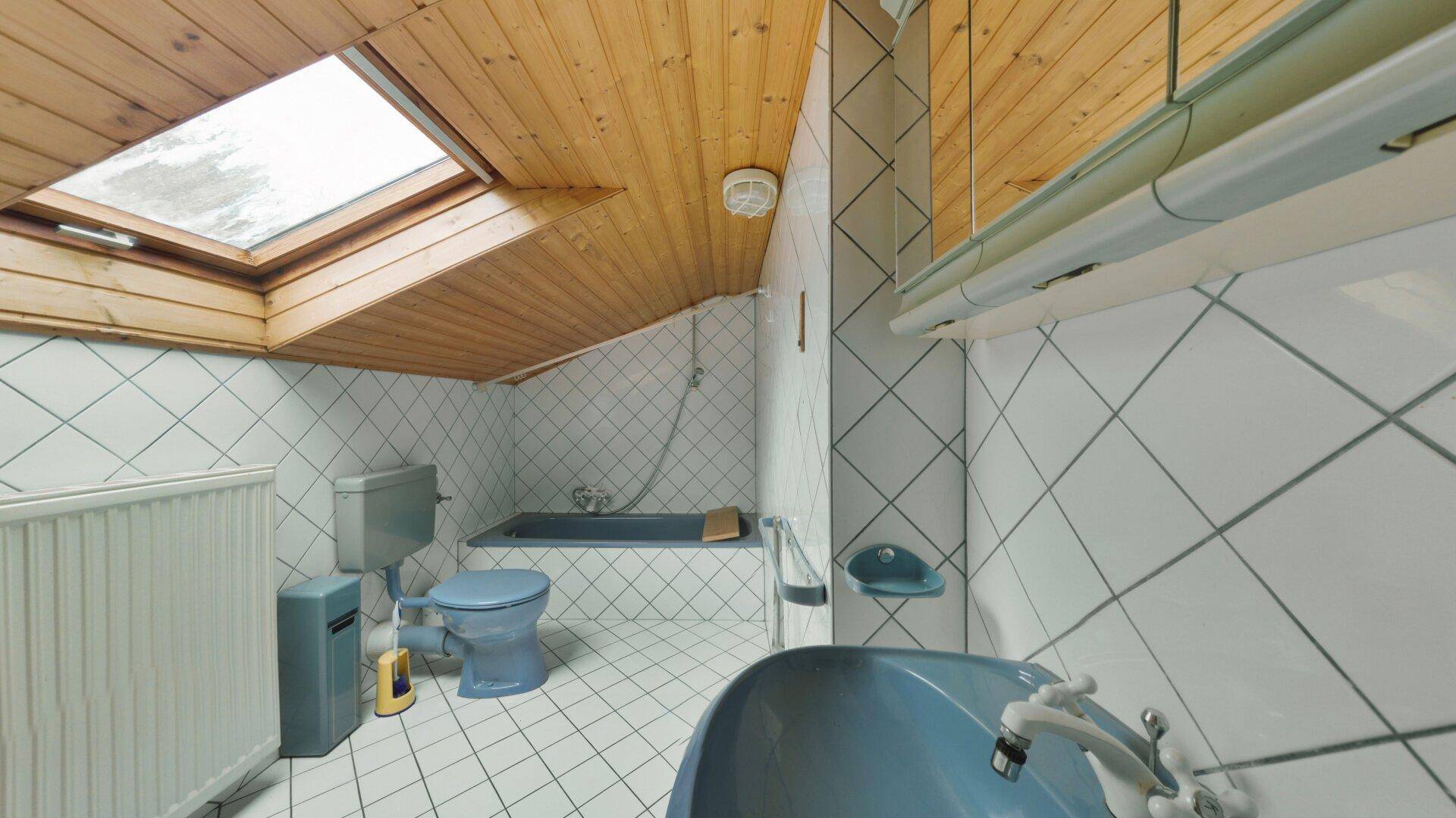 Badezimmer im Dachgeschoss mit Badewanne, Toilette und Dachfenster, hell gefliest.