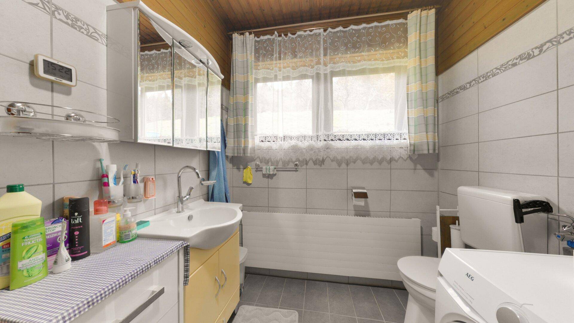 Funktionales Badezimmer mit Waschbecken, Toilette und Waschmaschine, hell gefliest und mit Fenster.