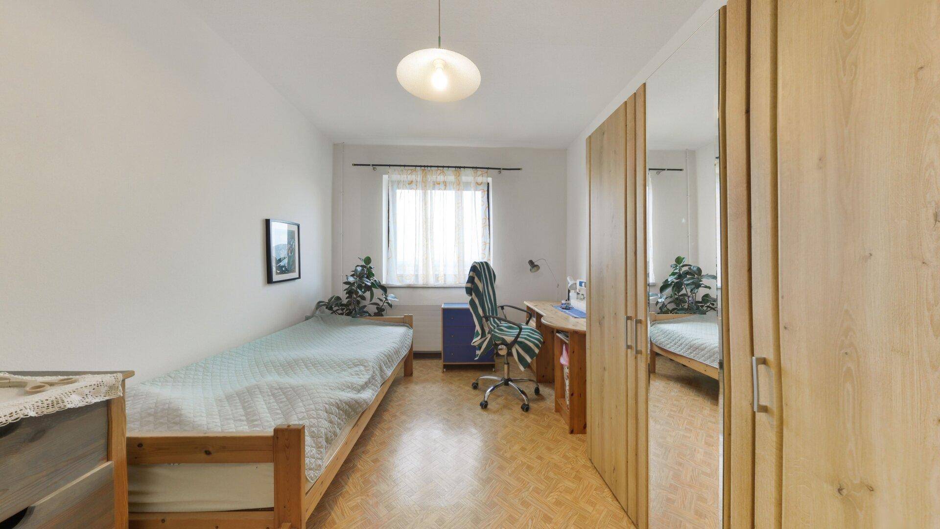 Helles Schlafzimmer mit Einzelbett, Schreibtisch und Spiegelschrank, ideal als Kinder- oder Gästezimmer.