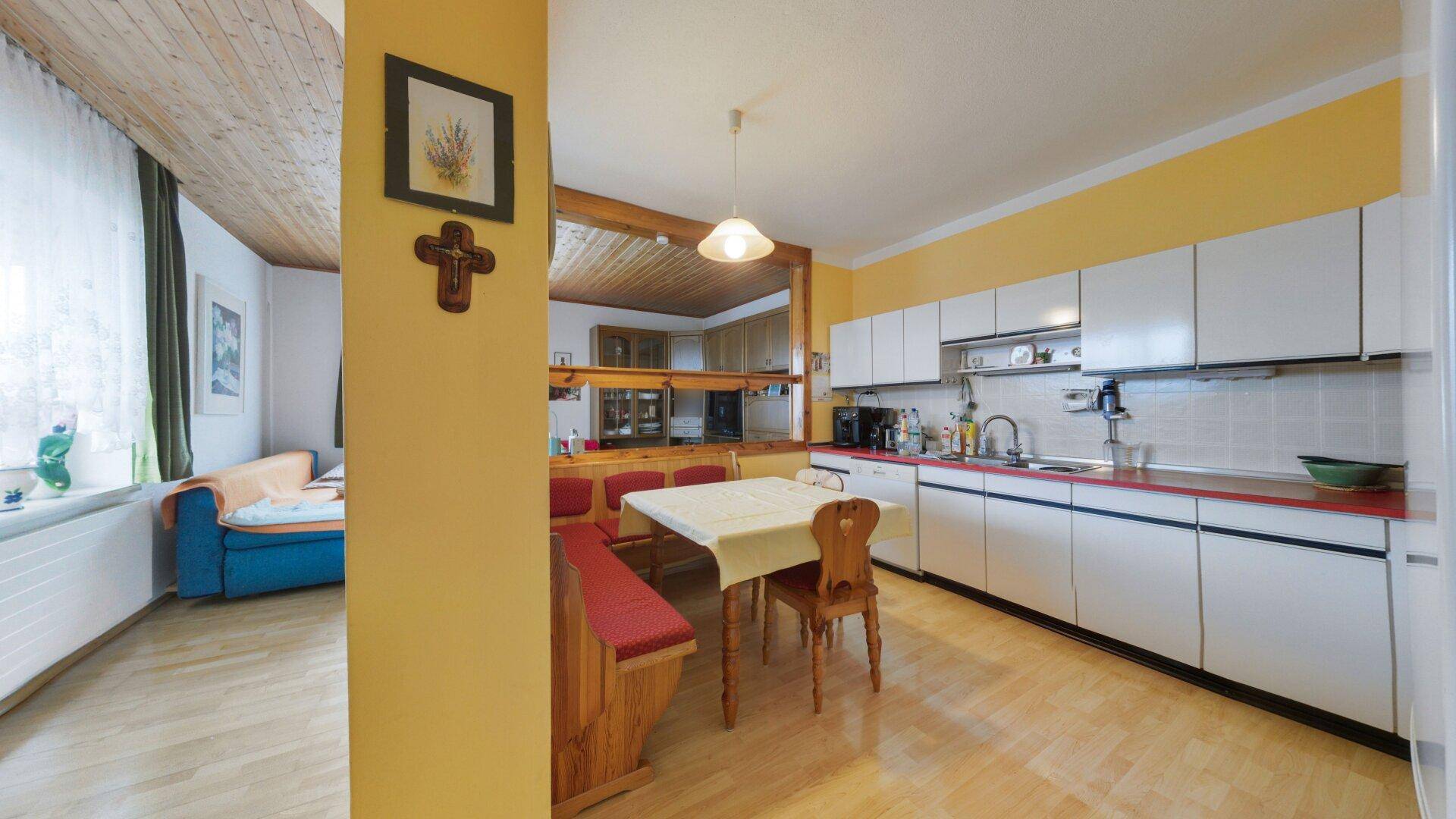 Traditionelle Küche mit Essecke, weißen Schränken und Holzdecke, verbunden mit dem Wohnbereich.
