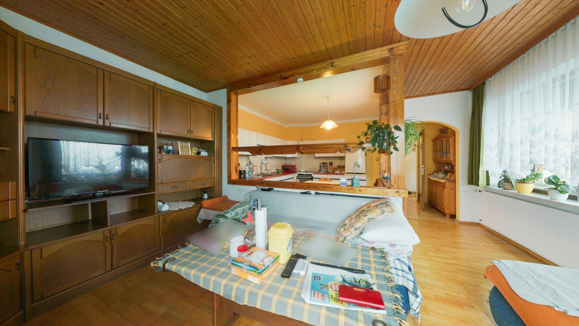 Gemütliches Wohnzimmer mit Holzdecke und Durchreiche zur Küche, bietet viel Stauraum.