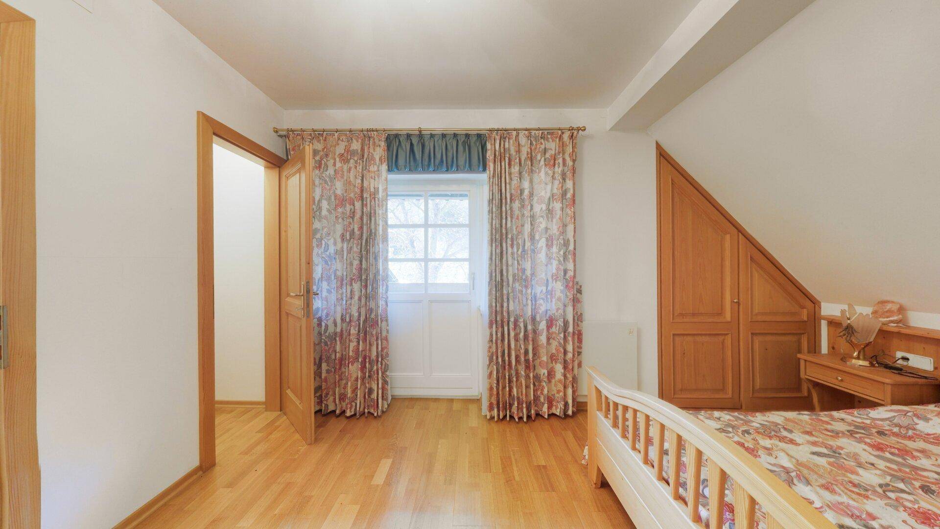 Schlafzimmer mit Holzbett, Parkettboden und schrägen Wänden unter dem Dach.