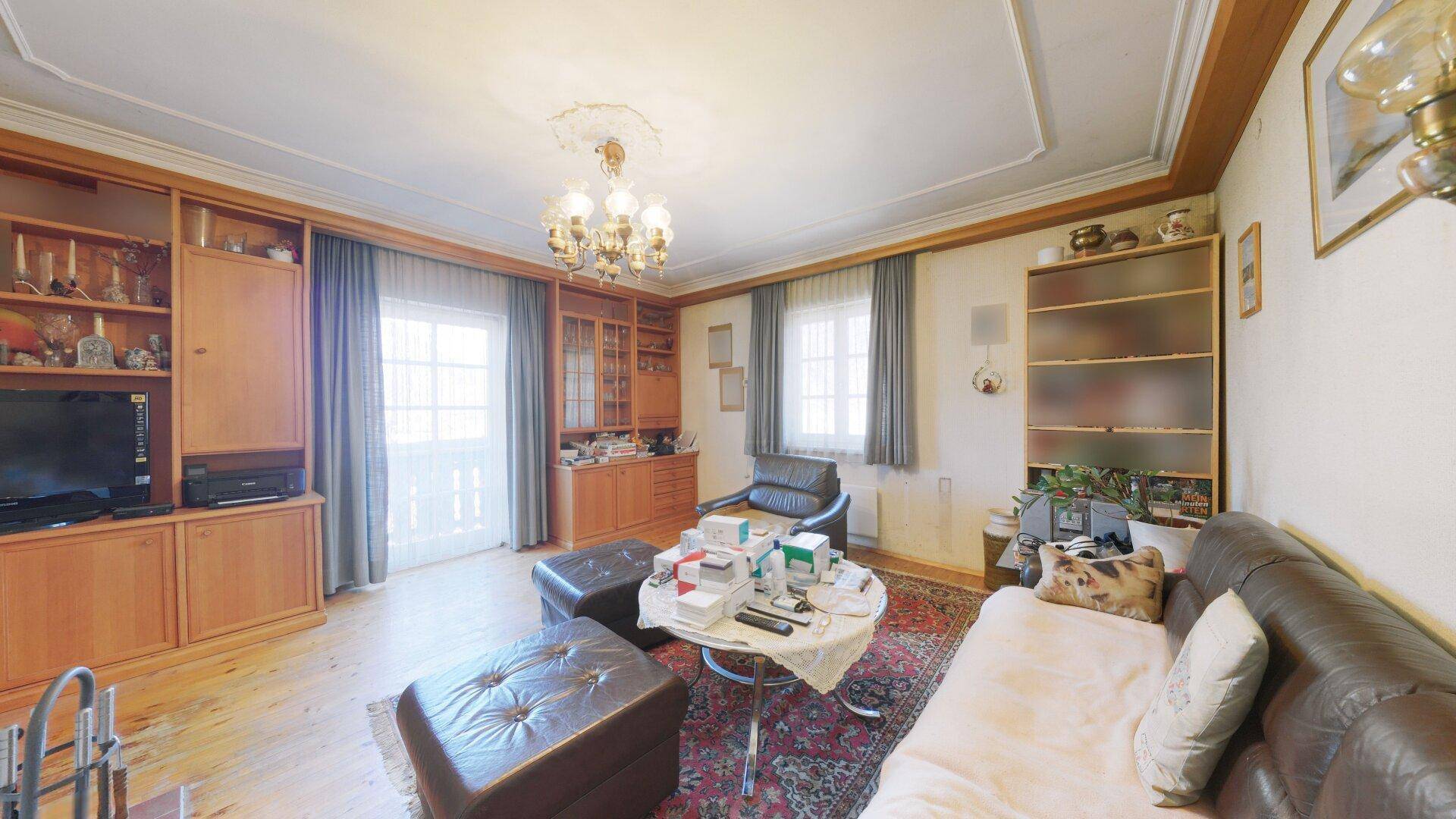 Gemütliches Wohnzimmer mit Ledersofa, Holzeinbauten und Zugang zu einem Balkon.