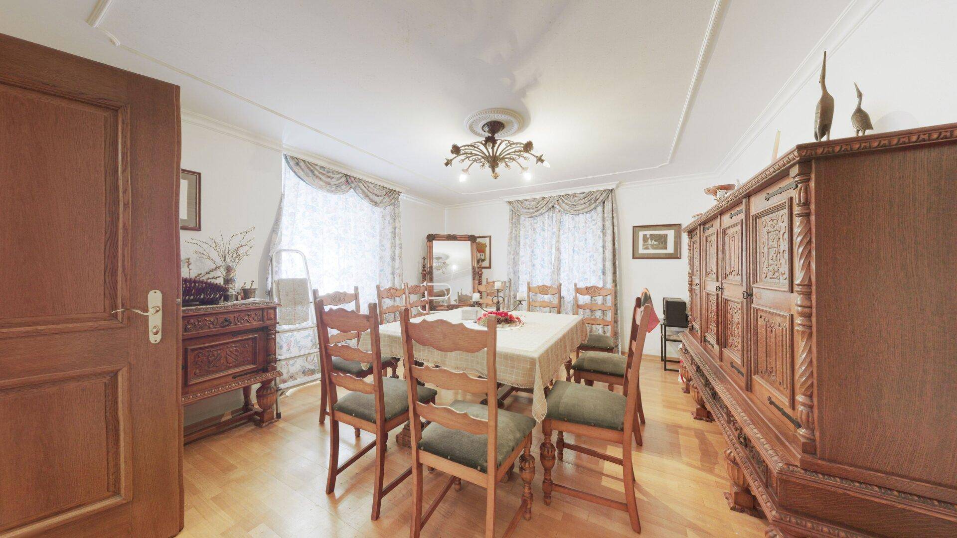 Elegantes Esszimmer mit großem Holztisch, antiken Möbeln und Kronleuchter.