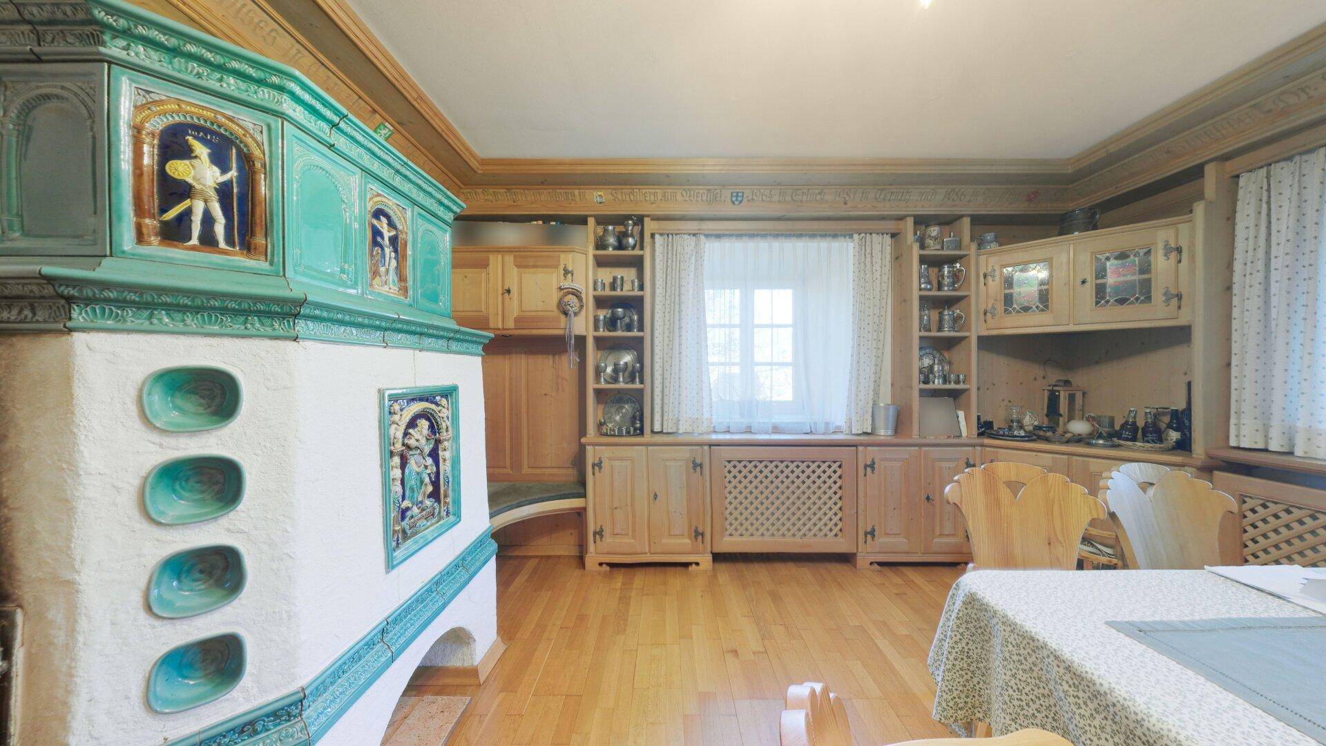 Geräumiger Wohnbereich mit traditionellem Kachelofen, Holzboden und Einbauschränken.