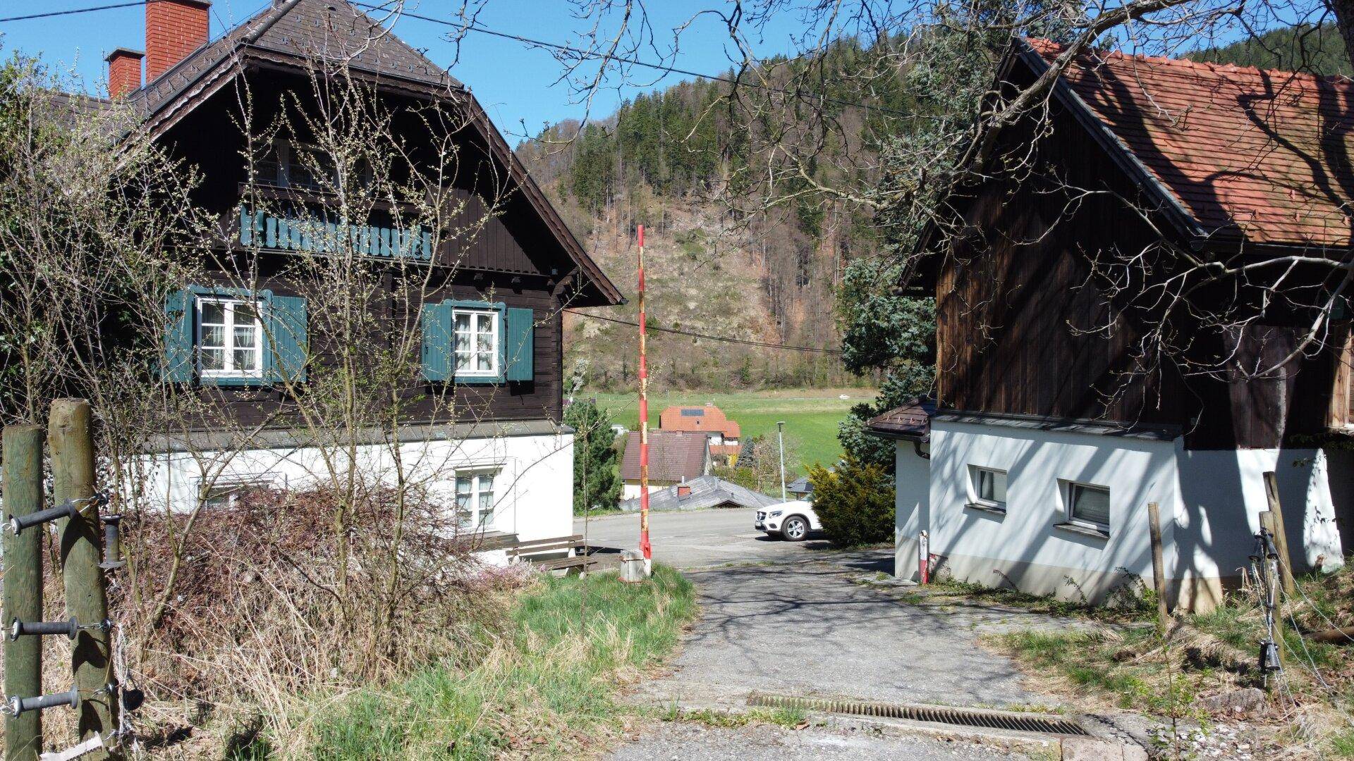Zwei traditionelle Gebäude mit Holzelementen und einem Zufahrtsweg in ländlicher Umgebung.