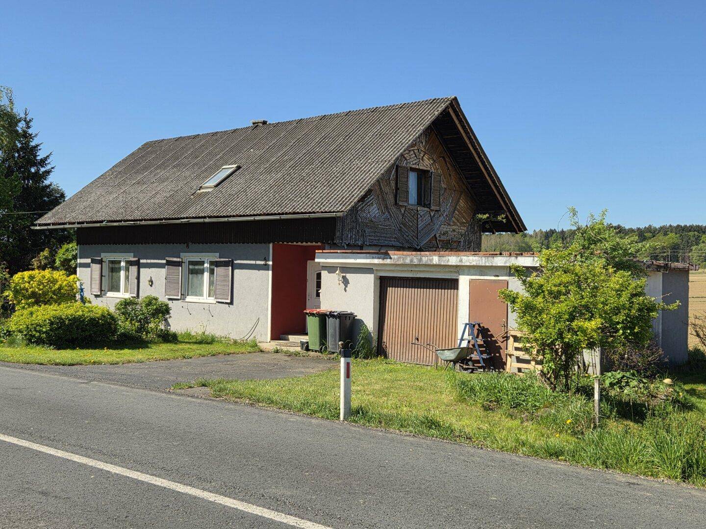 Ländliches Wohnhaus mit Satteldach, integrierter Garage und angrenzendem Feld unter blauem Himmel.