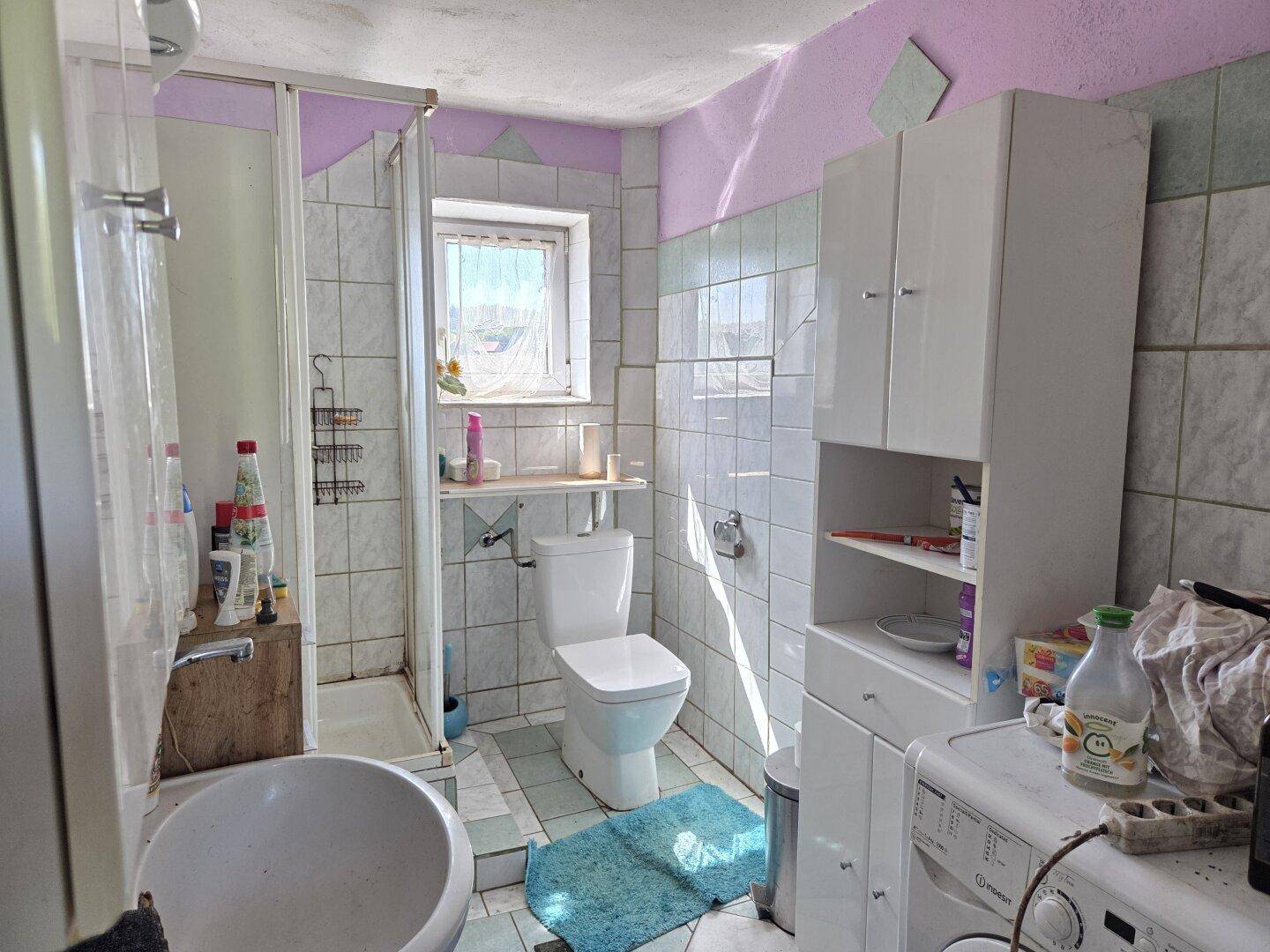 Badezimmer mit Dusche, WC, Waschmaschine und Fliesen in Pastellfarben.