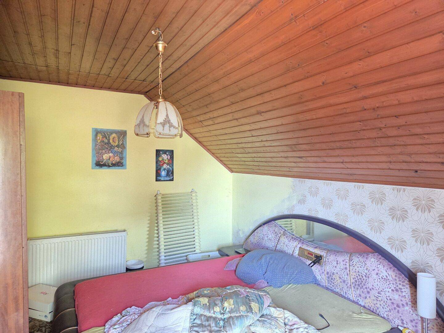 Schlafzimmer mit schräger Holzdecke, gelben Wänden und traditioneller Einrichtung.