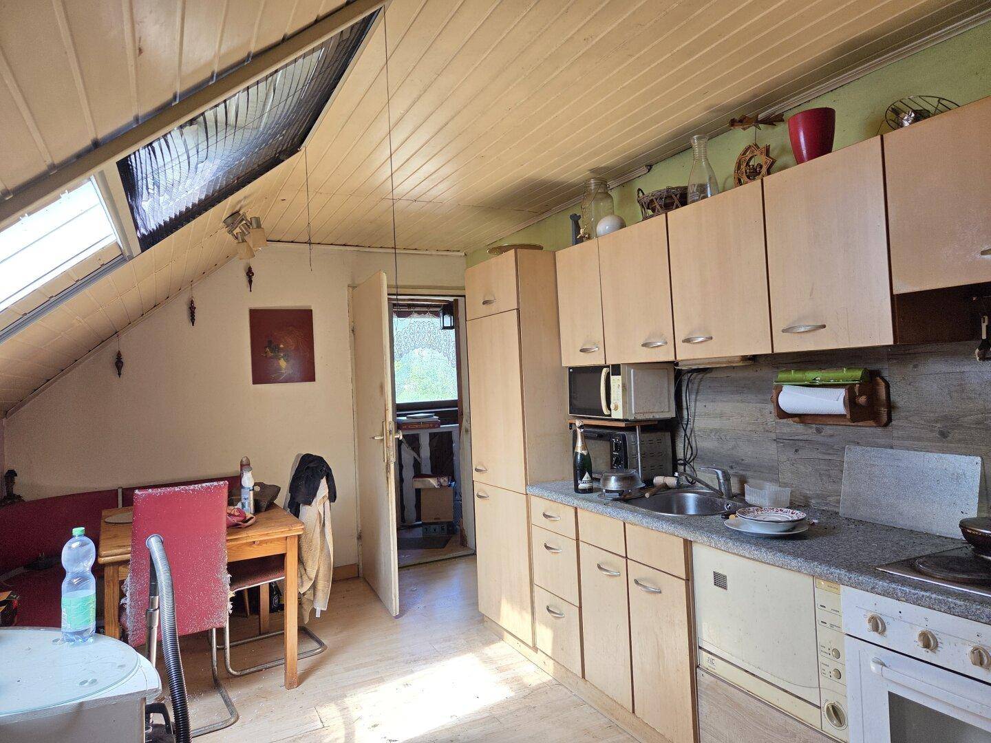 Kleine Küche mit Dachfenster, Holzeinbauten und Essbereich unter schräger Decke.