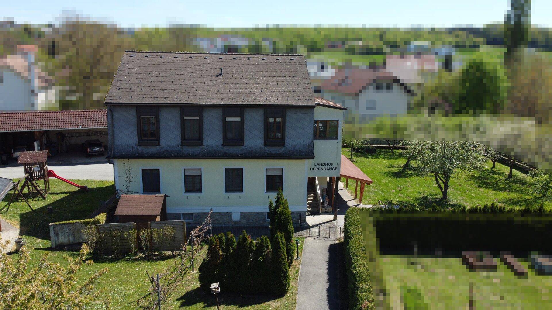 Vorderansicht des Wohngebäudes mit Spielplatz, gepflegtem Gartenweg und Hecken in ländlicher Lage.