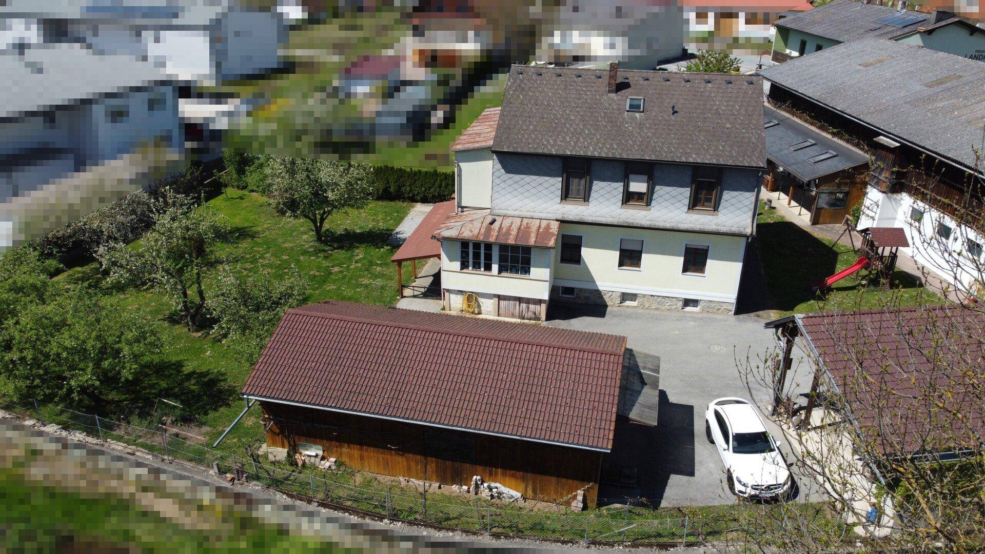 Ansicht des Wohnhauses mit Nebengebäude, Parkplatz und weitläufigen Grünflächen in der Umgebung.