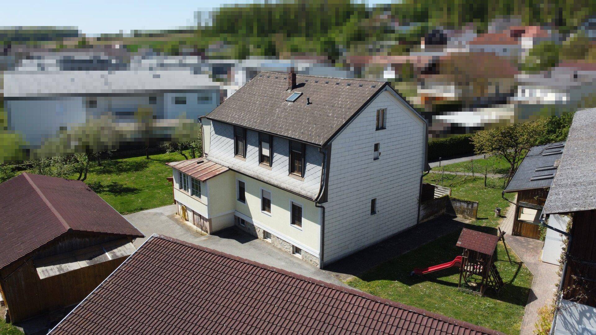 Wohngebäude mit Spielplatz im Garten, umgeben von Grünflächen und weiteren Nebengebäuden.