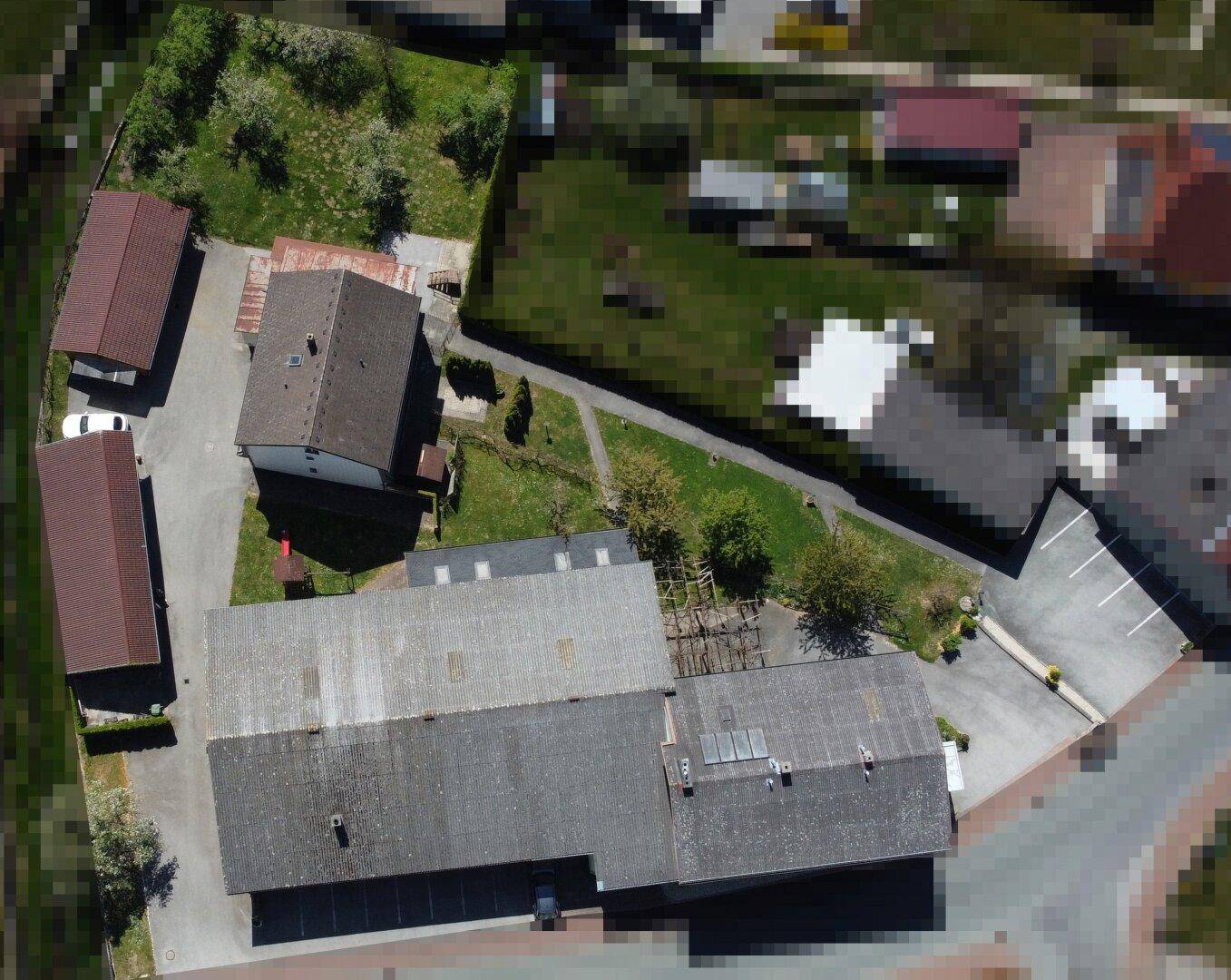 Draufsicht des Anwesens mit Gebäuden, Grünflächen, Parkmöglichkeiten und Solaranlage auf einem Dach.