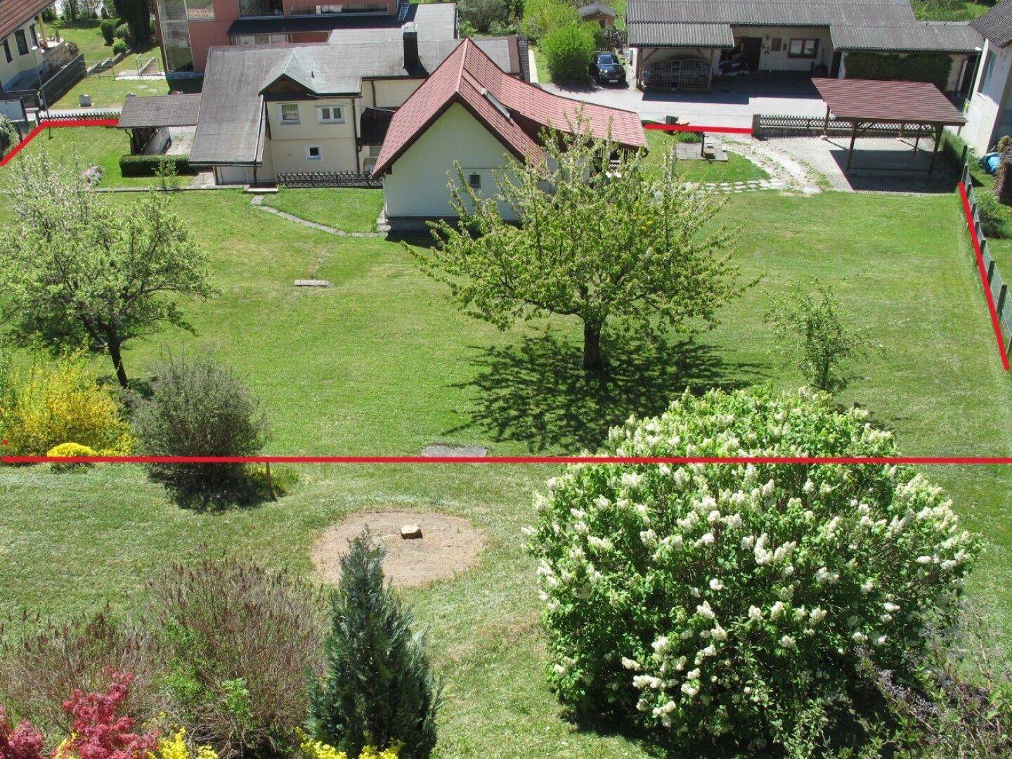 Großer grüner Garten mit Rasenfläche, Bäumen und Sträuchern, umgeben von Wohnhäusern in einer Wohngegend.
