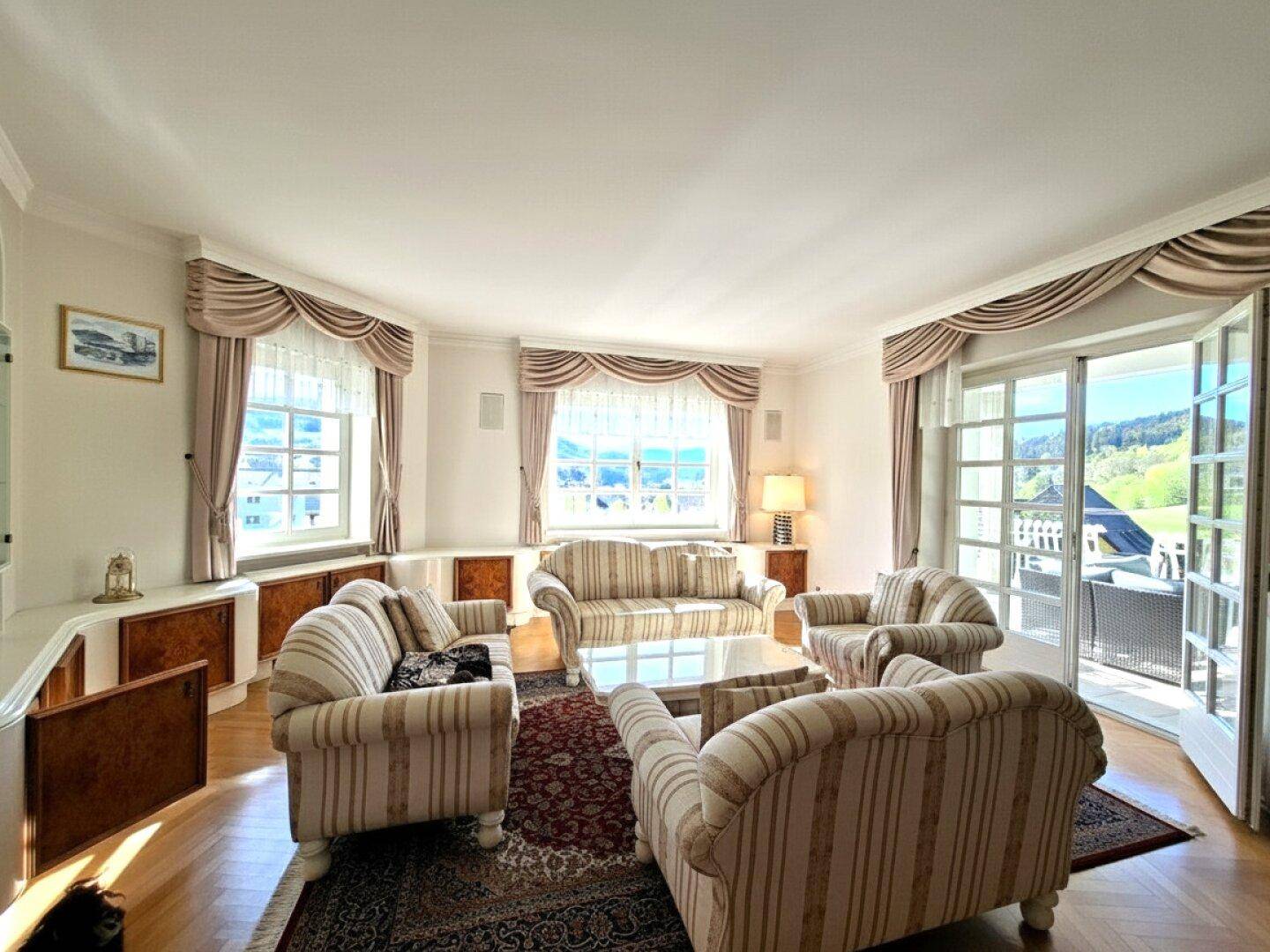 Geräumiges Wohnzimmer mit bequemen Sofas, Parkettboden und Zugang zu einem Balkon mit Aussicht.